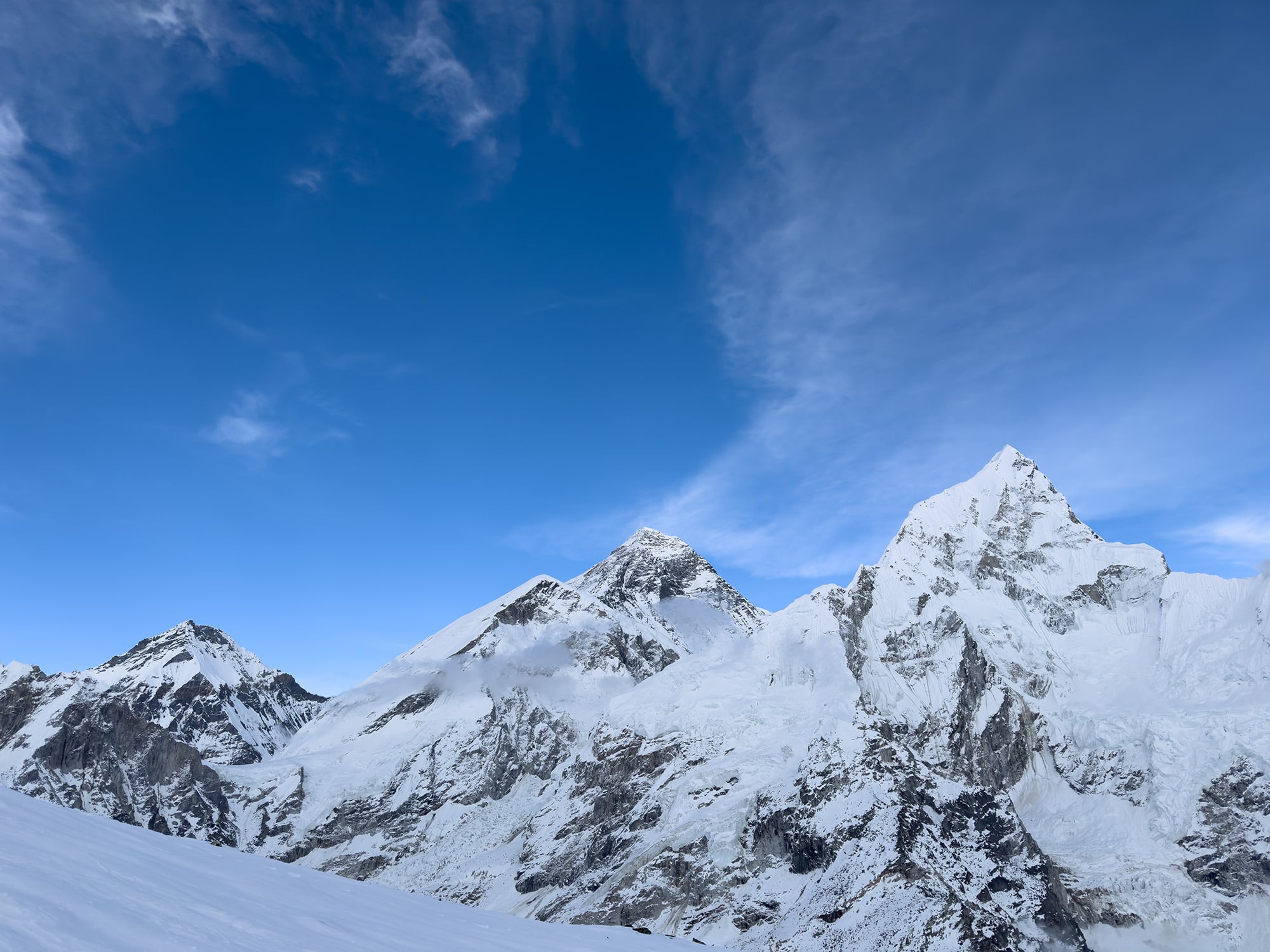 Everest covered in snow, with its towering peaks glistening against the clear blue sky, offering a majestic and awe-inspiring view in the heart of the Himalayas.