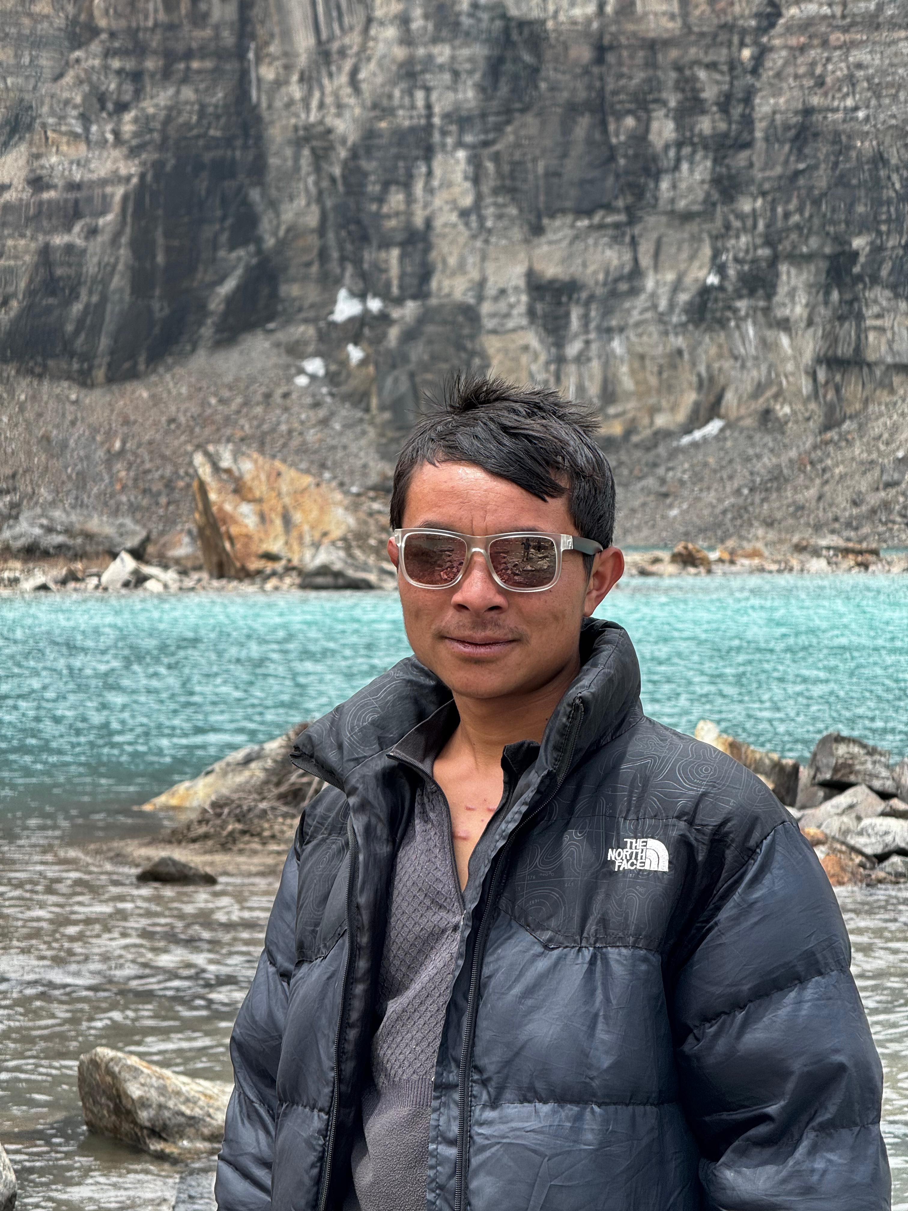 Sabin Sherpa with sunglasses posing in the Kanchenjunga Region, capturing the stunning mountain backdrop and the spirit of adventure in Eastern Nepal.