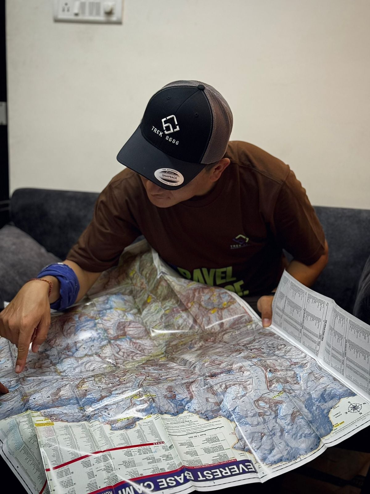 Boy wearing Trek 8586 cap studying Kanchenjunga Region map, ideal for trekking in Eastern Nepal with a reliable trekking agency.